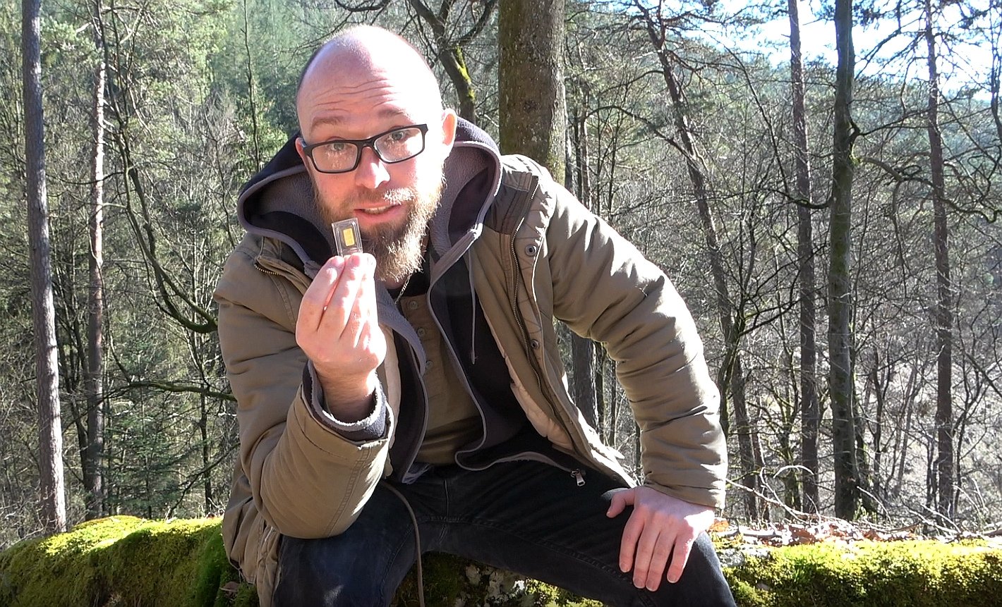 Marco Eitelmann hält symbolisch einen 1 Gramm Goldbarren nach oben und fragt woher das Gold kommt